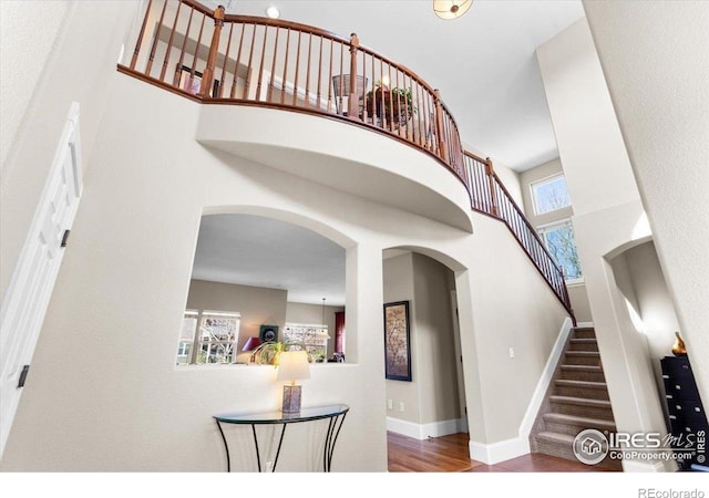 interior space featuring baseboards, wood finished floors, a towering ceiling, and arched walkways