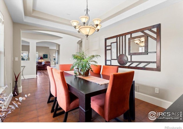 dining room with a tray ceiling, arched walkways, baseboards, a notable chandelier, and tile patterned flooring