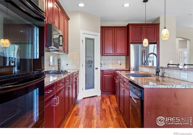 kitchen with light wood-type flooring, reddish brown cabinets, a sink, and black appliances