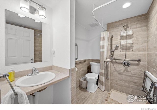 2417 15th Ave, Longmont, CO 80503 - bathroom featuring a tile shower, a wainscoted wall, toilet, a sink, and tile walls