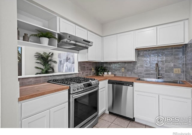 kitchen featuring wooden counters, under cabinet range hood, stainless steel appliances, open shelves, and a sink