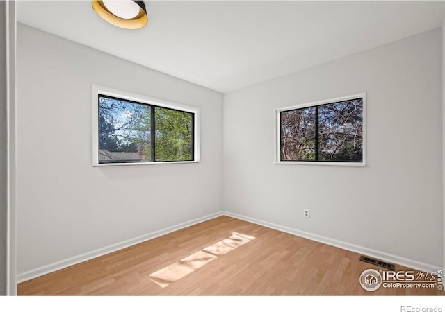 unfurnished room with wood finished floors, visible vents, and baseboards
