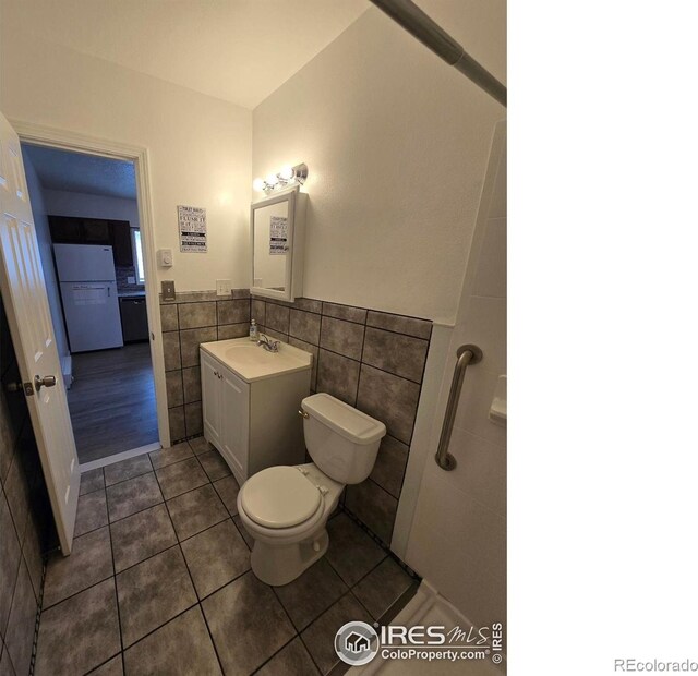 409 N 4th Ave, Sterling, CO 80751 - bathroom with tile walls, tile patterned floors, toilet, vanity, and a wainscoted wall