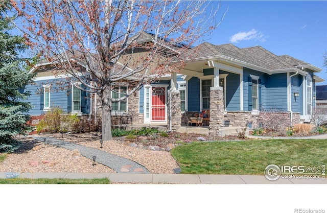 craftsman house featuring a porch, a front lawn, roof with shingles, and stone siding