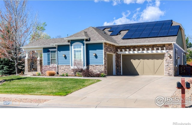 view of front of property with roof mounted solar panels, an attached garage, stone siding, and driveway