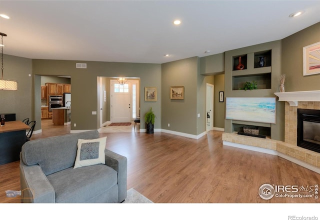 living area with light wood-style floors, a tile fireplace, baseboards, visible vents, and recessed lighting