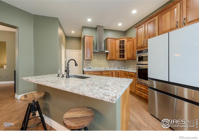 kitchen featuring wall chimney range hood, light wood-style flooring, a sink, and freestanding refrigerator