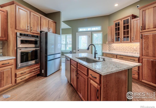 kitchen featuring light wood finished floors, stainless steel appliances, a sink, tasteful backsplash, and glass insert cabinets
