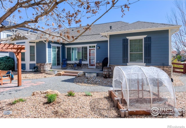 rear view of property featuring a patio area, stone siding, fence, and a shingled roof