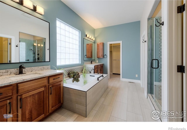 bathroom featuring a shower stall, two vanities, a sink, and a spacious closet