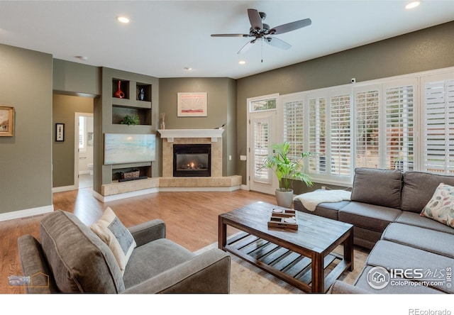 living area with a tiled fireplace, a ceiling fan, recessed lighting, and light wood-style flooring