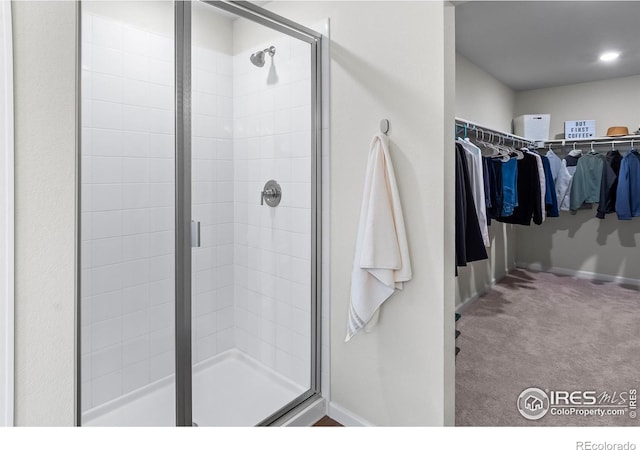 bathroom featuring a walk in closet, baseboards, and a stall shower