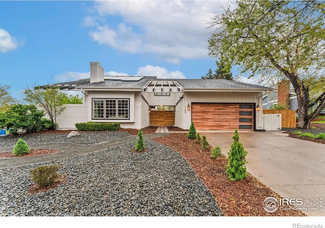 view of front facade featuring an attached garage, a chimney, fence, concrete driveway, and solar panels