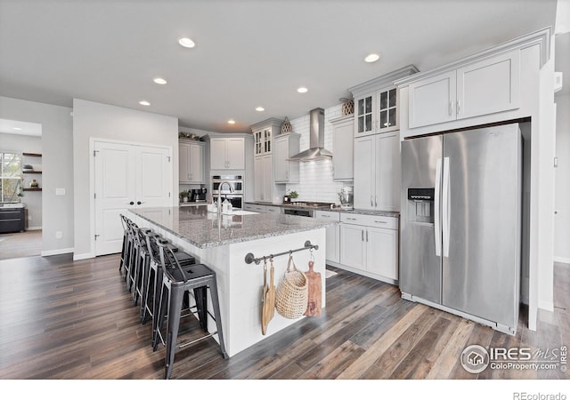 kitchen featuring dark wood finished floors, wall chimney range hood, baseboards, and stainless steel appliances