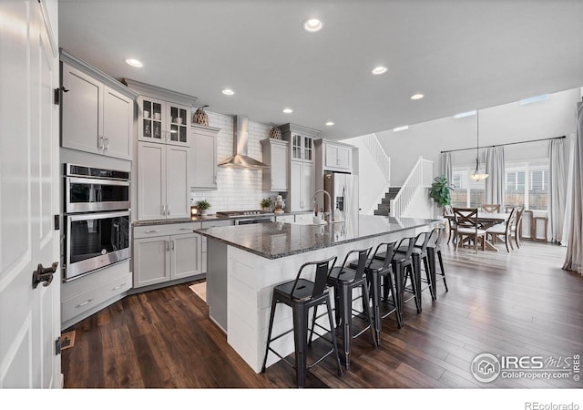 kitchen with wall chimney exhaust hood, stainless steel appliances, dark wood-style floors, and a breakfast bar area