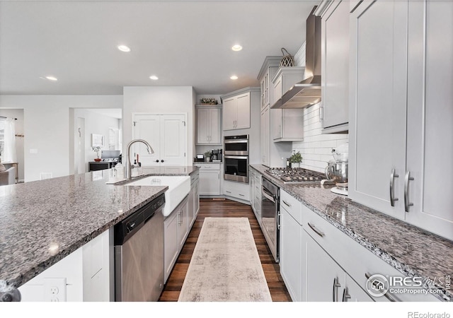 kitchen with dark wood-style flooring, a sink, wall chimney exhaust hood, appliances with stainless steel finishes, and recessed lighting