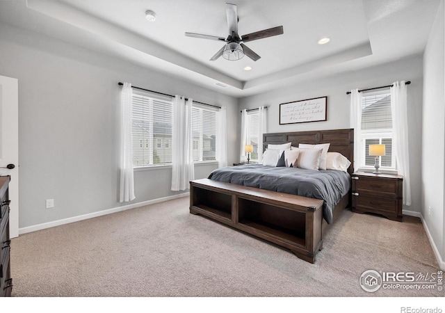 bedroom featuring recessed lighting, a tray ceiling, baseboards, light colored carpet, and multiple windows
