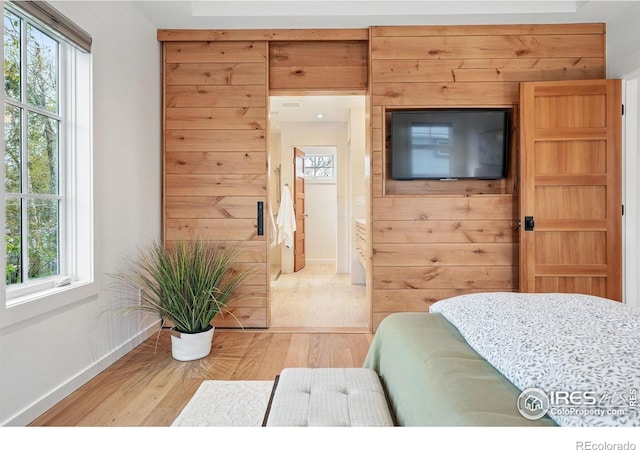 bedroom featuring baseboards, wood walls, and light wood-style flooring