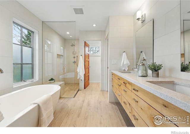 bathroom featuring a walk in shower, a freestanding bath, a wealth of natural light, and wood finished floors