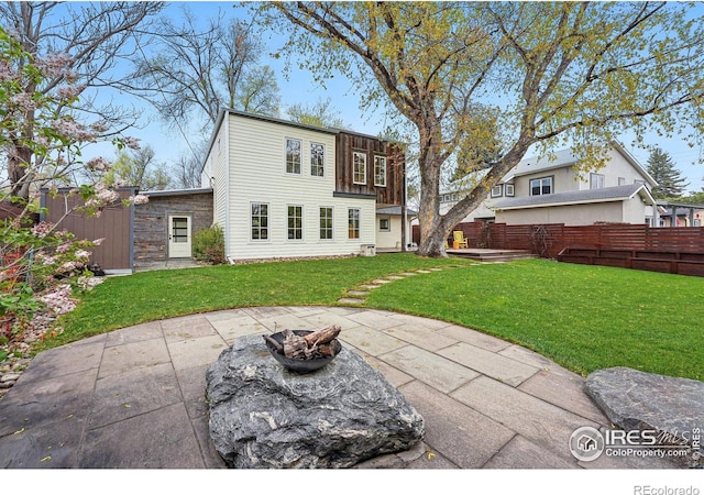 rear view of property featuring a lawn, fence private yard, a patio area, and an outdoor fire pit