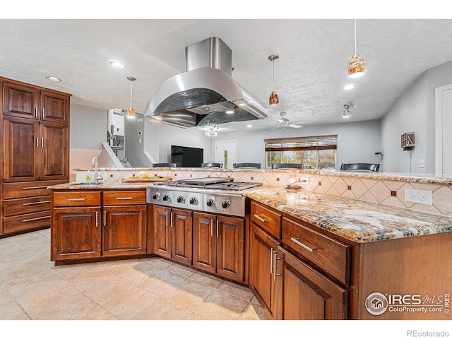 kitchen featuring light stone countertops, a ceiling fan, island range hood, stainless steel gas stovetop, and tasteful backsplash