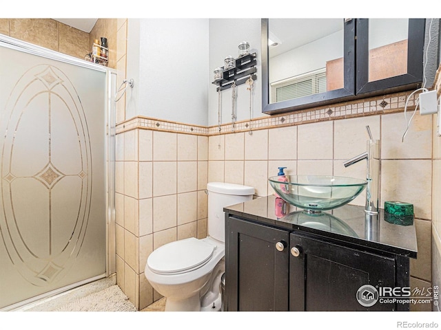 bathroom featuring tile walls, wainscoting, a stall shower, vanity, and toilet