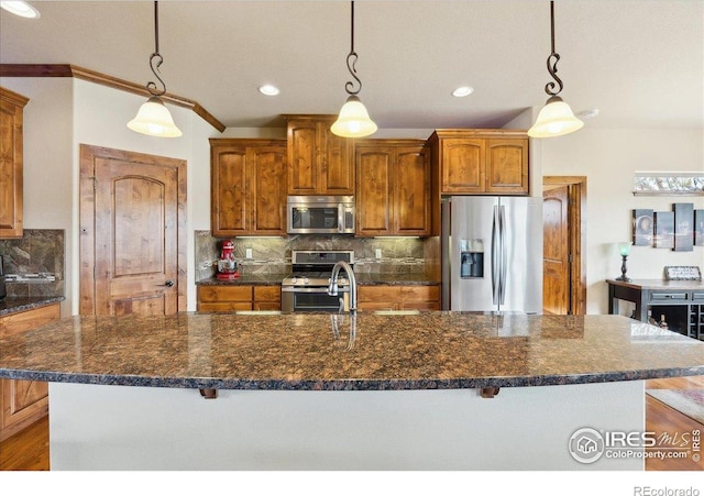 3560 Peruvian Torch Dr, Loveland, CO 80537 - kitchen featuring stainless steel appliances, brown cabinetry, tasteful backsplash, a kitchen island with sink, and hanging light fixtures