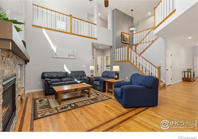 living room featuring a high ceiling, a brick fireplace, stairs, baseboards, and wood finished floors