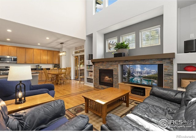 living area featuring recessed lighting, light wood-style flooring, a towering ceiling, and a lit fireplace