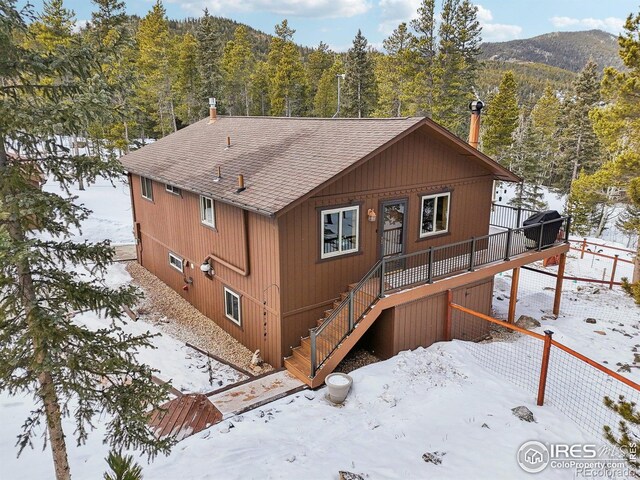 10649 Christopher Dr, Conifer, CO 80433 - snow covered back of property with roof with shingles, a deck with mountain view, a wooded view, and stairway