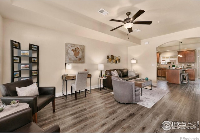 living area featuring ceiling fan, arched walkways, baseboards, dark wood-style flooring, and visible vents