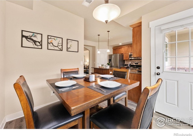 dining room with arched walkways, wood finished floors, visible vents, and baseboards