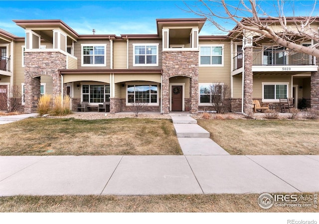 view of front of home featuring a front lawn, stone siding, and a balcony