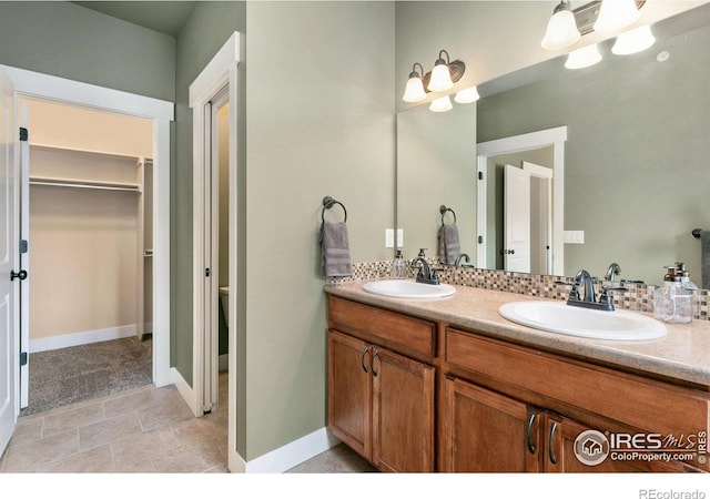 bathroom with tasteful backsplash, double vanity, a spacious closet, and a sink