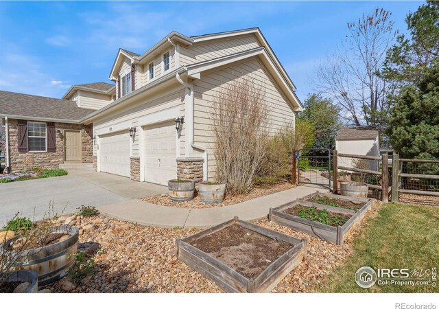 view of side of property featuring fence, an attached garage, stone siding, a garden, and driveway