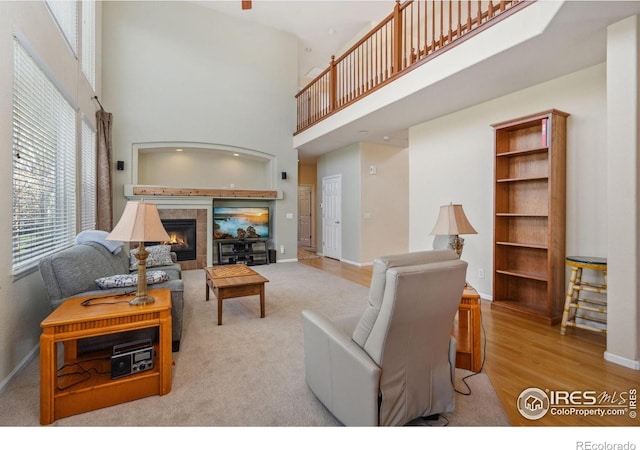 living room featuring a tiled fireplace, baseboards, a high ceiling, and wood finished floors