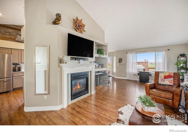 2190 Coyote Creek Dr, Fort Lupton, CO 80621 - living area with wood finished floors, a glass covered fireplace, baseboards, and high vaulted ceiling