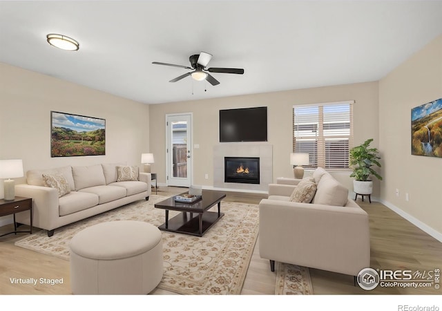 living area with baseboards, a ceiling fan, wood finished floors, and a fireplace