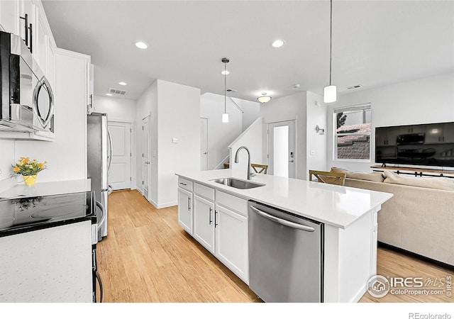 kitchen with light wood finished floors, stainless steel appliances, white cabinets, a sink, and an island with sink