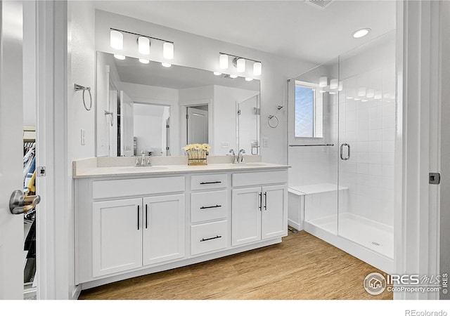 bathroom with double vanity, a shower stall, wood finished floors, and a sink