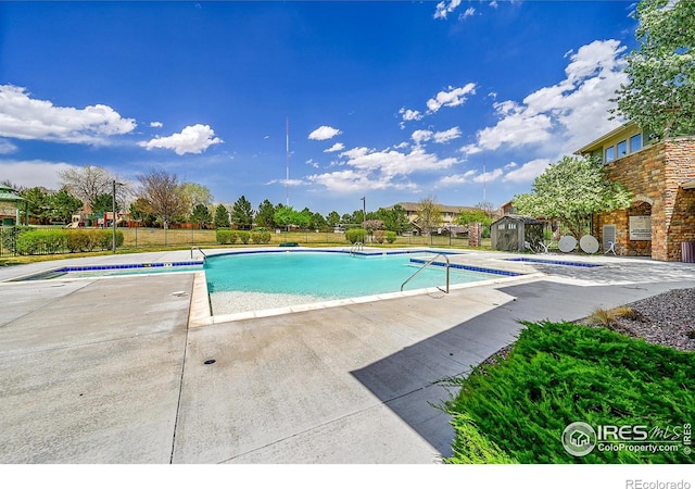 pool with an outdoor structure, a shed, a patio, and fence