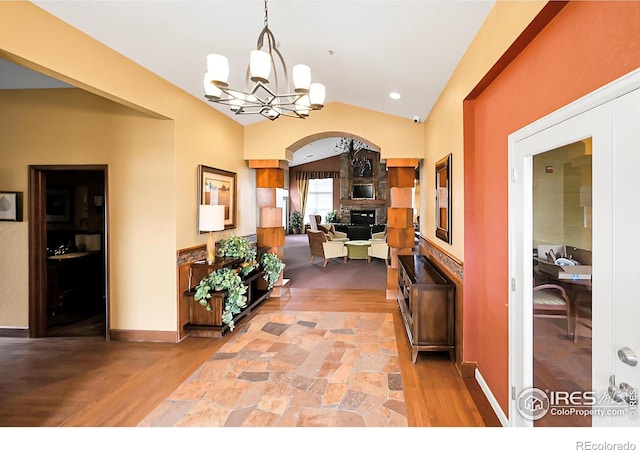 hallway featuring arched walkways, vaulted ceiling, a chandelier, and light wood-style flooring