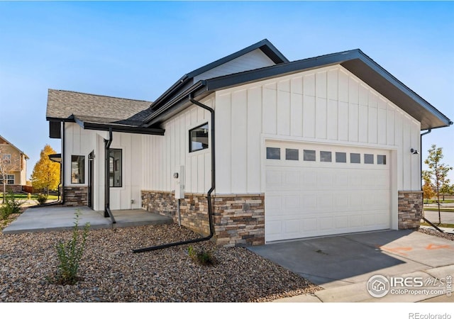view of front facade featuring board and batten siding, stone siding, concrete driveway, and a garage