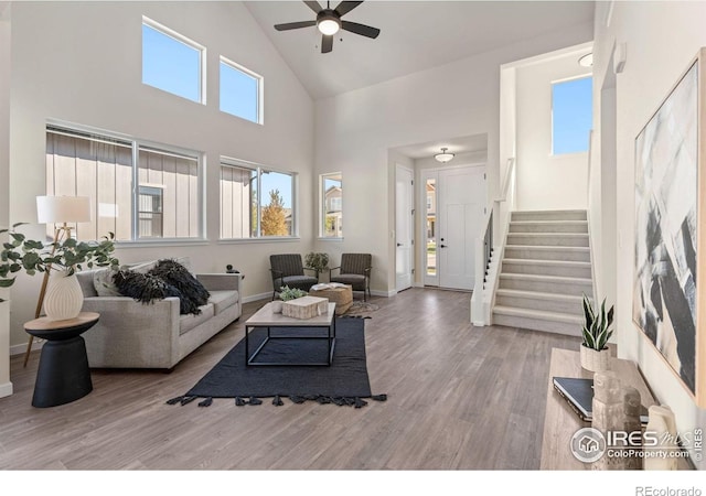 living room featuring high vaulted ceiling, wood finished floors, a ceiling fan, baseboards, and stairs
