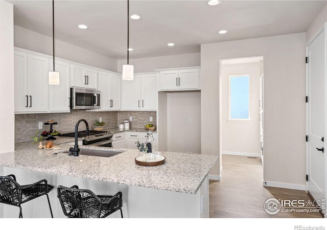 kitchen with backsplash, a sink, light wood-type flooring, a peninsula, and appliances with stainless steel finishes