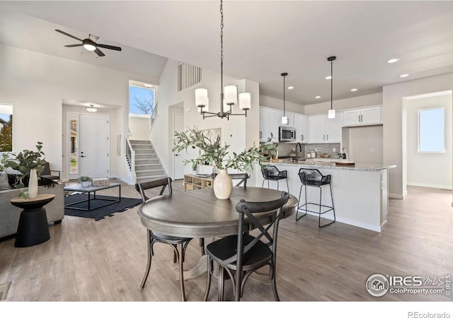 dining room featuring recessed lighting, light wood finished floors, baseboards, stairs, and ceiling fan with notable chandelier