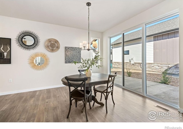 dining area with baseboards, wood finished floors, visible vents, and an inviting chandelier