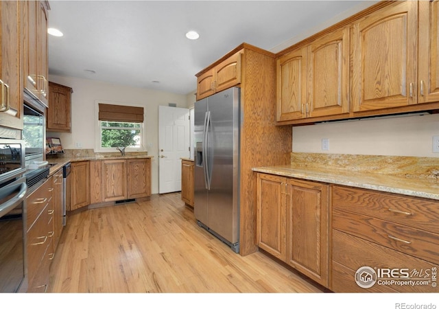 kitchen with light wood-style flooring, light stone counters, brown cabinets, and appliances with stainless steel finishes