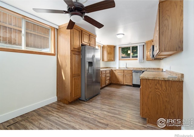 kitchen with a sink, baseboards, a ceiling fan, wood finished floors, and appliances with stainless steel finishes