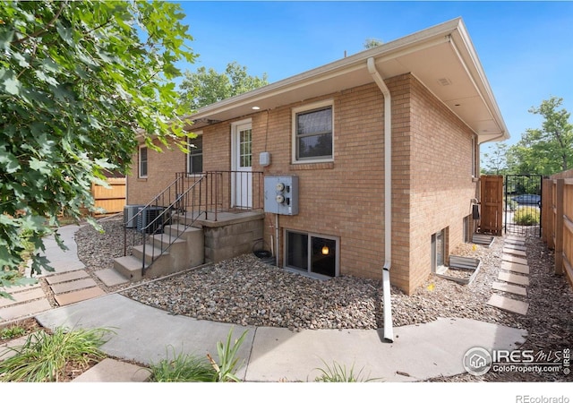 rear view of house with central air condition unit, brick siding, and fence